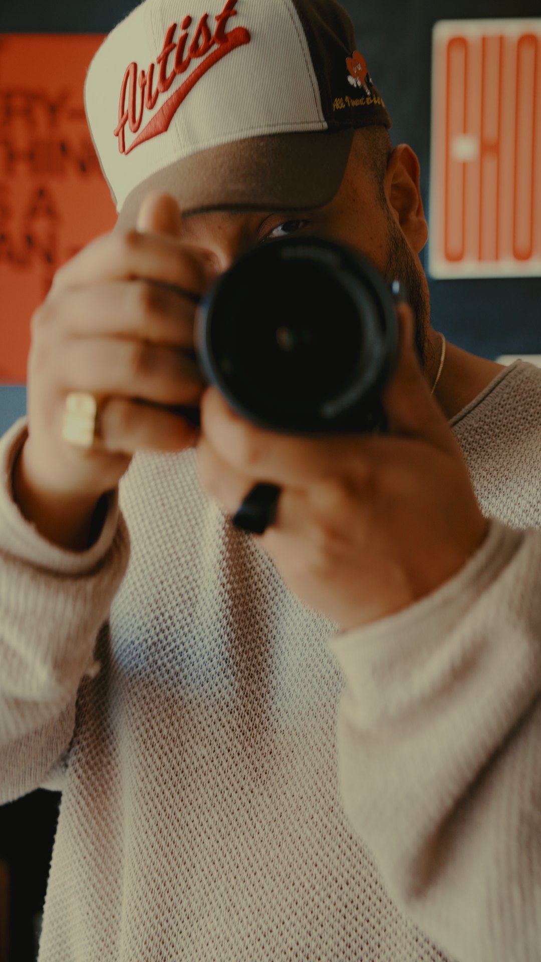 Jordan Ray behind a camera in an Artist cap, one eye on the lens